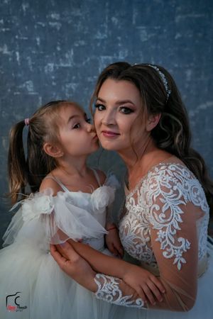 Emotional wedding day moment between bride and young flower girl in matching white dresses.