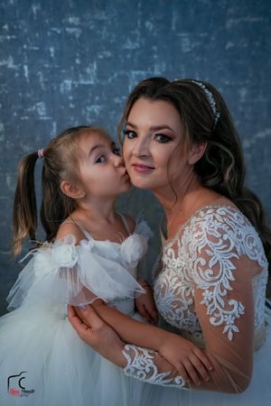 Candid portrait of bride and flower girl sharing loving moment against textured blue wall.