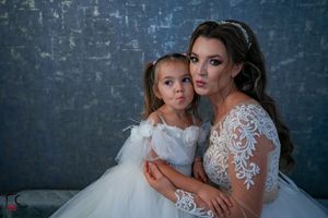 Tender embrace between bride wearing lace gown and young flower girl in white dress.