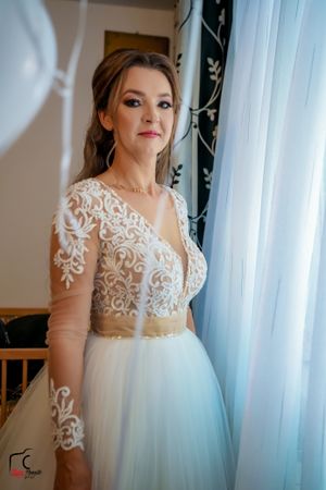 Ethereal wedding dress with sheer lace overlay photographed against white curtains.