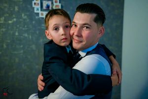 A tender embrace shared during a formal occasion against a blue textured wall.