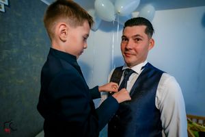 A heartwarming moment as a child helps with formal attire preparations in a room with balloons.
