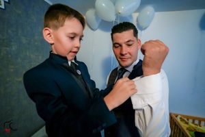 A young boy helps adjust a navy blue tie on a formal outfit during a special occasion.