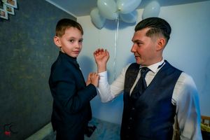 Two people in formal attire share a tender moment at a celebration with blue balloon decor.