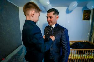 Two people in formal attire interact warmly at an event with balloons in the background.