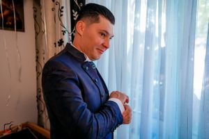 Person in formal navy suit stands by window with natural lighting.