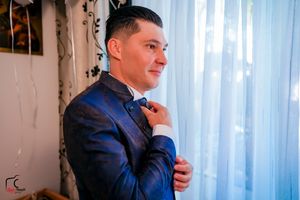 Person wearing a dark suit poses near window with white curtains.