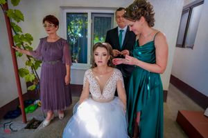 Wedding party helping with final dress preparations in a sunlit room.