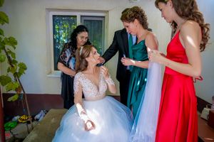 Candid wedding preparation scene with bridesmaids helping the bride get ready in a sunlit room.