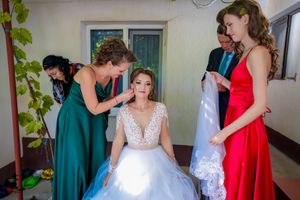 Wedding day getting ready moment with bridesmaids in emerald and red dresses assisting the bride.