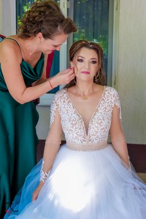Elegant bride in a white lace ballgown receives final styling touches from her wedding party.