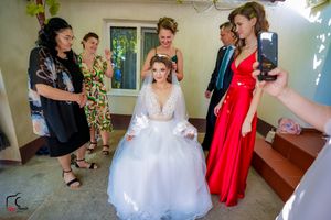 Wedding preparation scene showing final touches being made to a bride's elegant white gown and accessories.