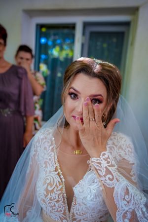 Candid moment of bride covering face with hand while wearing elegant lace gown.