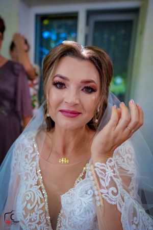 Bride with glamorous makeup wearing pearl jewelry and white lace wedding dress.