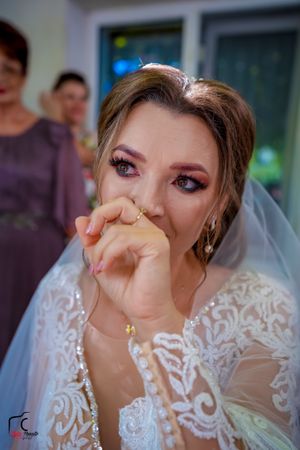 Emotional bride wiping tears while wearing an intricately detailed lace wedding dress and veil.