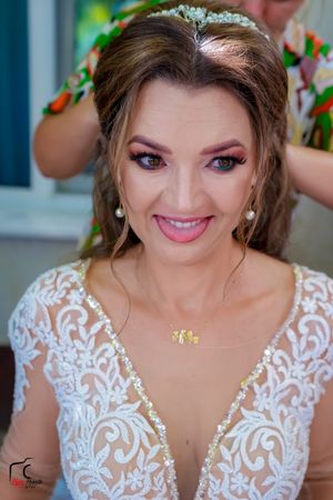 Joyful bride in a white lace V-neck wedding gown smiling at the camera during preparation.