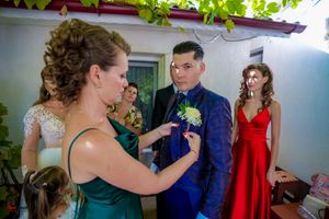 Wedding party members helping with formal attire preparations in a light-filled room.