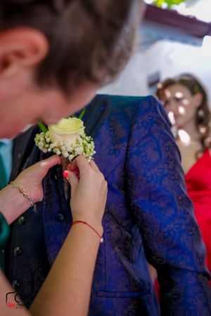 Close-up shot of hands pinning a white floral boutonniere onto a navy blue suit jacket at a formal event.