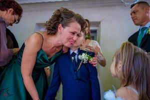 Wedding attendant in teal helping adjust formal attire on a young member of the wedding party.