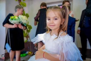 A young attendee in a white dress participates in wedding celebrations.