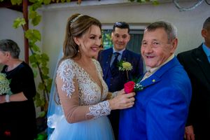 A bride in a lace dress shares a tender dance moment with a guest in a bright blue suit at a wedding reception.