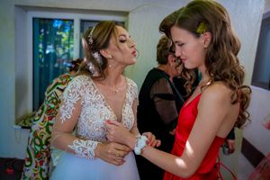A bride in a lace dress and guest in red share an intimate conversation at a wedding.