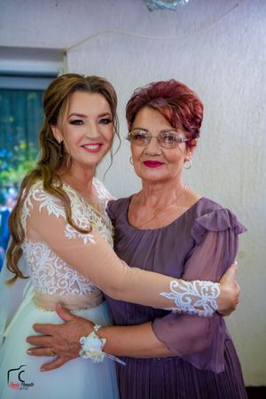 A bride in a white lace dress shares an emotional moment with a woman in a purple dress during a wedding celebration.