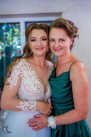 Two wedding attendants share an intimate moment in white lace and emerald green dresses.