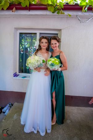 Wedding attendees in formal dresses pose together under green vine canopy.