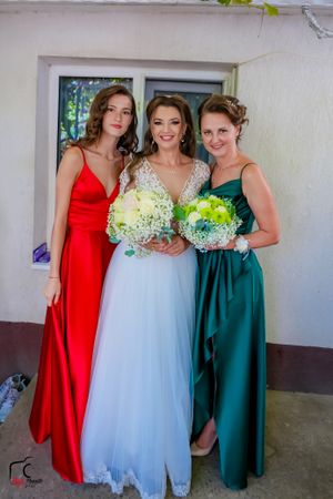 Wedding party members in formal attire pose for photos against white wall with window.