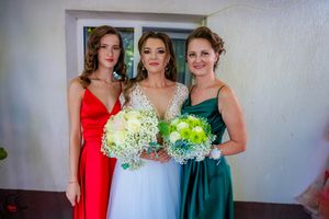 Wedding party members in elegant dresses pose together against white wall background.