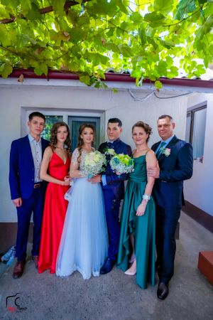 Wedding group photo with mix of formal attire in navy, red, and emerald green against white backdrop.