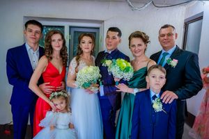 Extended wedding party lined up for formal photos against white wall with hanging vines.