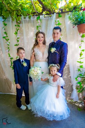 Wedding party poses outdoors with bride in white gown and others in navy blue attire against vine-covered wall.