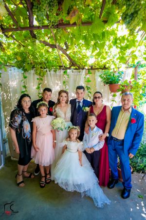 Extended family wedding photo under vine-covered patio with natural lighting.