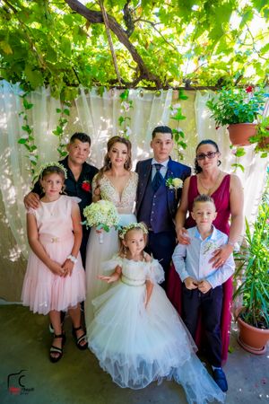 Wedding group portrait with children in white dresses under garden arbor.