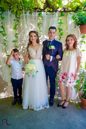 Family wedding portrait against white curtains and hanging greenery.