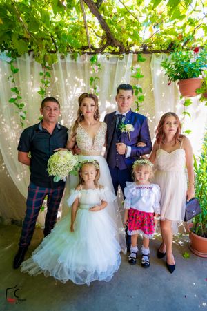 Wedding party poses in a garden setting with greenery and white curtains as backdrop.