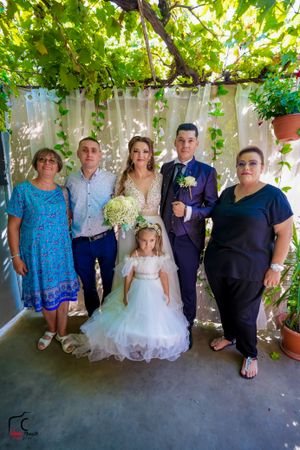 Group portrait under green pergola with people in formal blue and white attire.