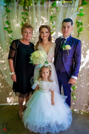 Formal group photo under vine-covered pergola with white tulle dress and navy suit.