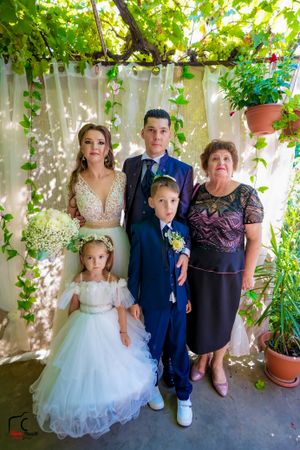 Family photo under vine-covered pergola with formal attire and white tulle dress.