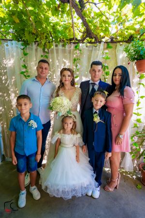 Group photo under vine-covered pergola with people in coordinated blue and white formal wear.