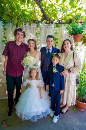 Wedding party poses under leafy pergola with children in formal attire.