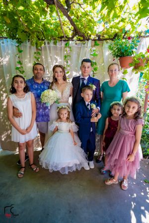 Group photo under a vine-covered pergola with children and adults in formal attire.