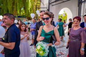 A woman in an emerald green dress holds a bouquet of white and green flowers at an outdoor event.