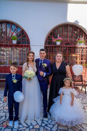 Wedding party members in formal wear pose against church exterior with red metal gates.