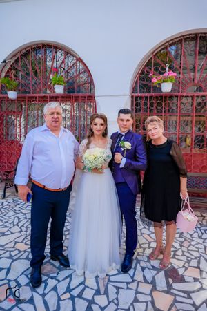 Wedding party poses outside church with ornate red metal gates and stone paved ground.