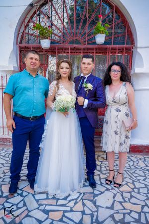 Wedding party poses in different combinations against white wall with red ornamental ironwork.