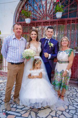 Wedding party poses in front of decorative red iron gate and stone patio during outdoor celebration.