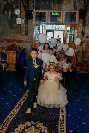 Young attendees walk across a blue carpeted floor with decorative Greek key pattern border.